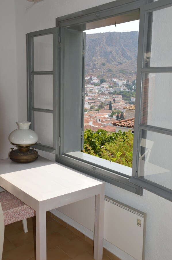 A room with a white table and a window overlooking a town and mountains. - Hydra studio house with amazing harbour views (Hydra Town, Hydra)