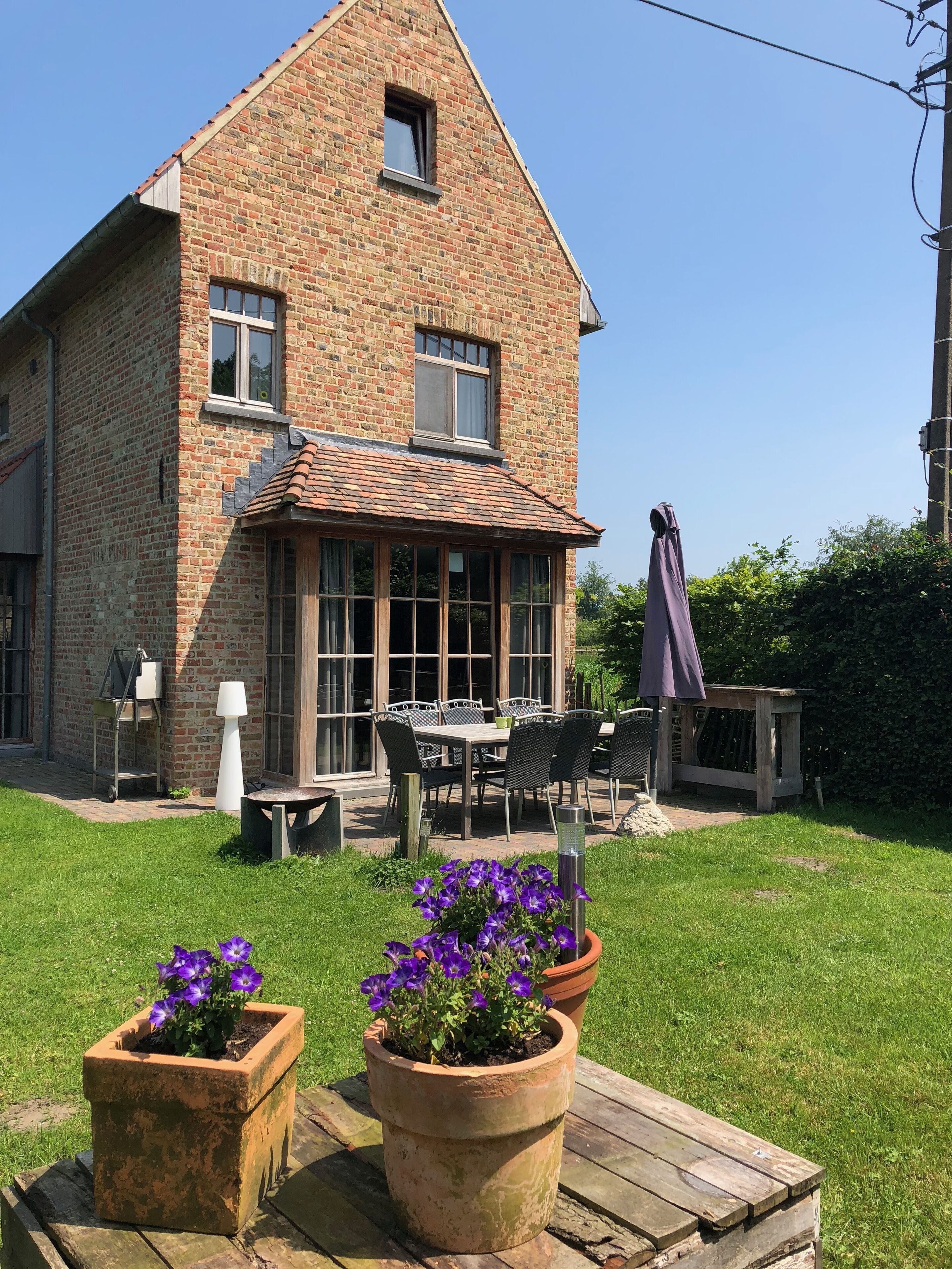 A brick house with a large window, a patio with outdoor furniture, and potted flowers.