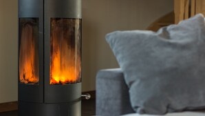 A modern fireplace with a glass front, a sofa with a grey cushion, and a wooden staircase in the background.