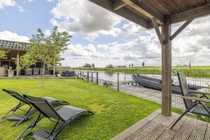 Ein überdachter Außenbereich mit Holzterrasse, Rasenfläche und Blick auf einen Fluss.