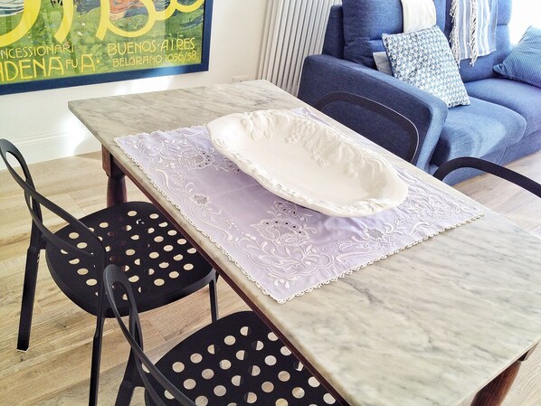 Un coin repas avec une table en marbre, deux chaises noires dotées d’ouvertures circulaires et une assiette blanche posée sur un chemin de table violet.
