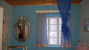 Un dormitorio con una cama, una ventana con cortinas, un espejo y una mesita.