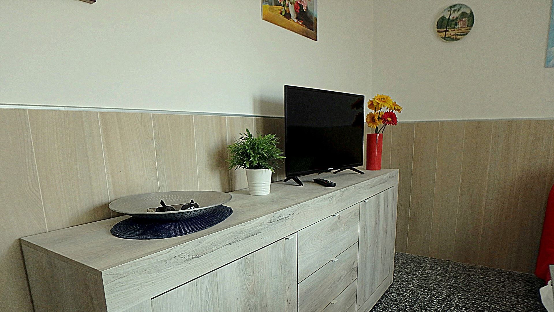 Una recepción con un televisor de pantalla plana, una planta en maceta y un florero con flores.