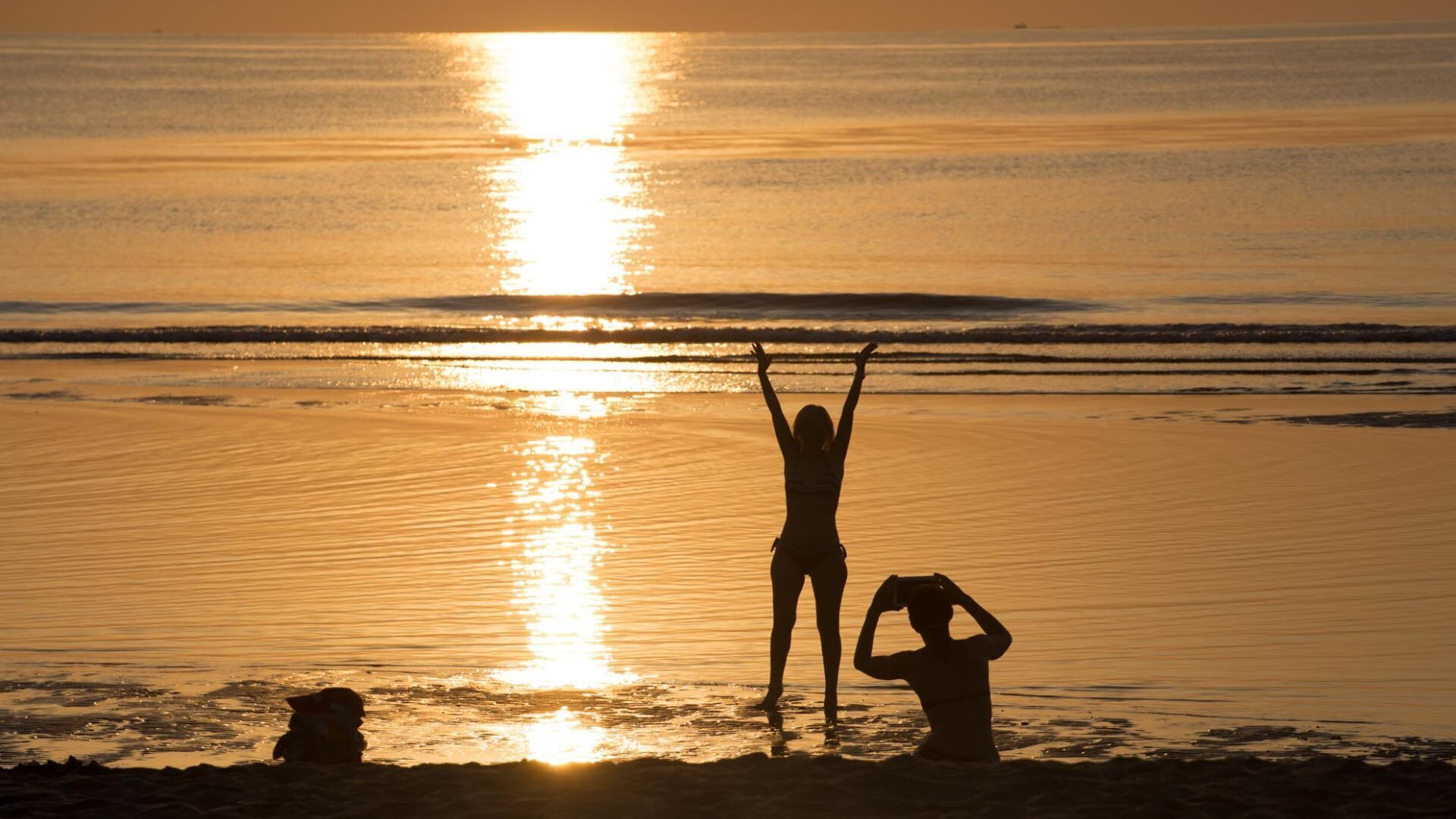 Cena de praia com duas pessoas silhuetadas contra o pôr do sol.