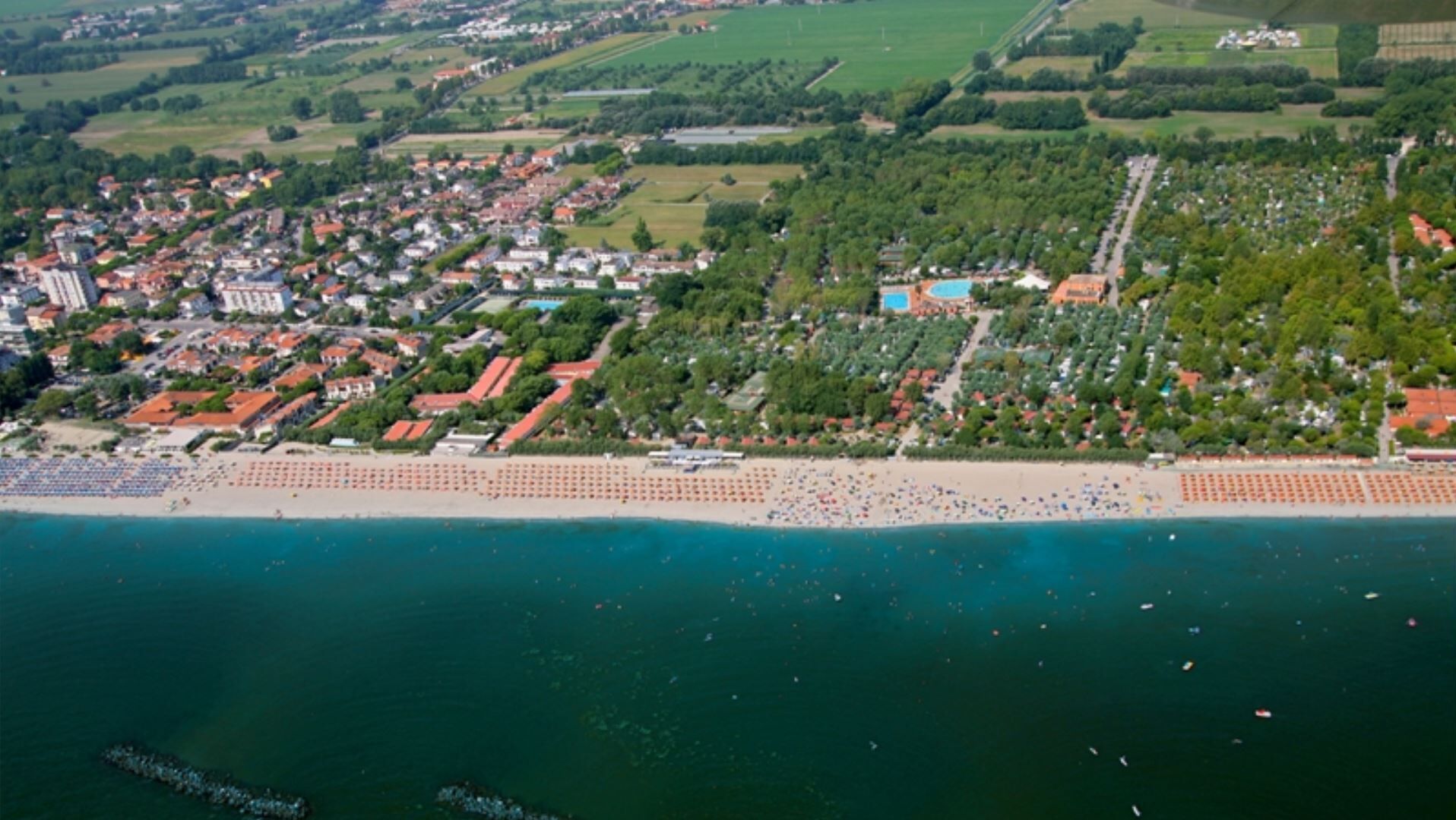 Vista aérea de un pueblo costero con playa, zonas residenciales y un gran edificio con piscina.