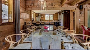 Ein Holzblockbau-Innenraum mit Esstisch, Stühlen, einer Chandelier-Leuchte und einer Küchenzeile.