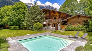 Eine Holzhütte mit Pool, umgeben von üppiger Vegetation und Bergen.