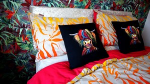 A bed with a colorful bedspread and two pillows with a colorful animal design. - In Our Liverpool Home, 3 Bedrooms Sleeps 5 (Liverpool)