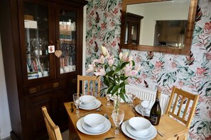 Une table à manger dressée avec de l’assiette blanche, des verres et un vase de fleurs.