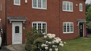 A two-story brick house with a front door, a small porch, and a garden with white flowers. - In Our Liverpool Home, 3 Bedrooms Sleeps 5 (Liverpool)
