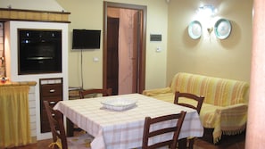 A compact living space with a dining table, chairs, a sofa, a television, and a kitchen area.
