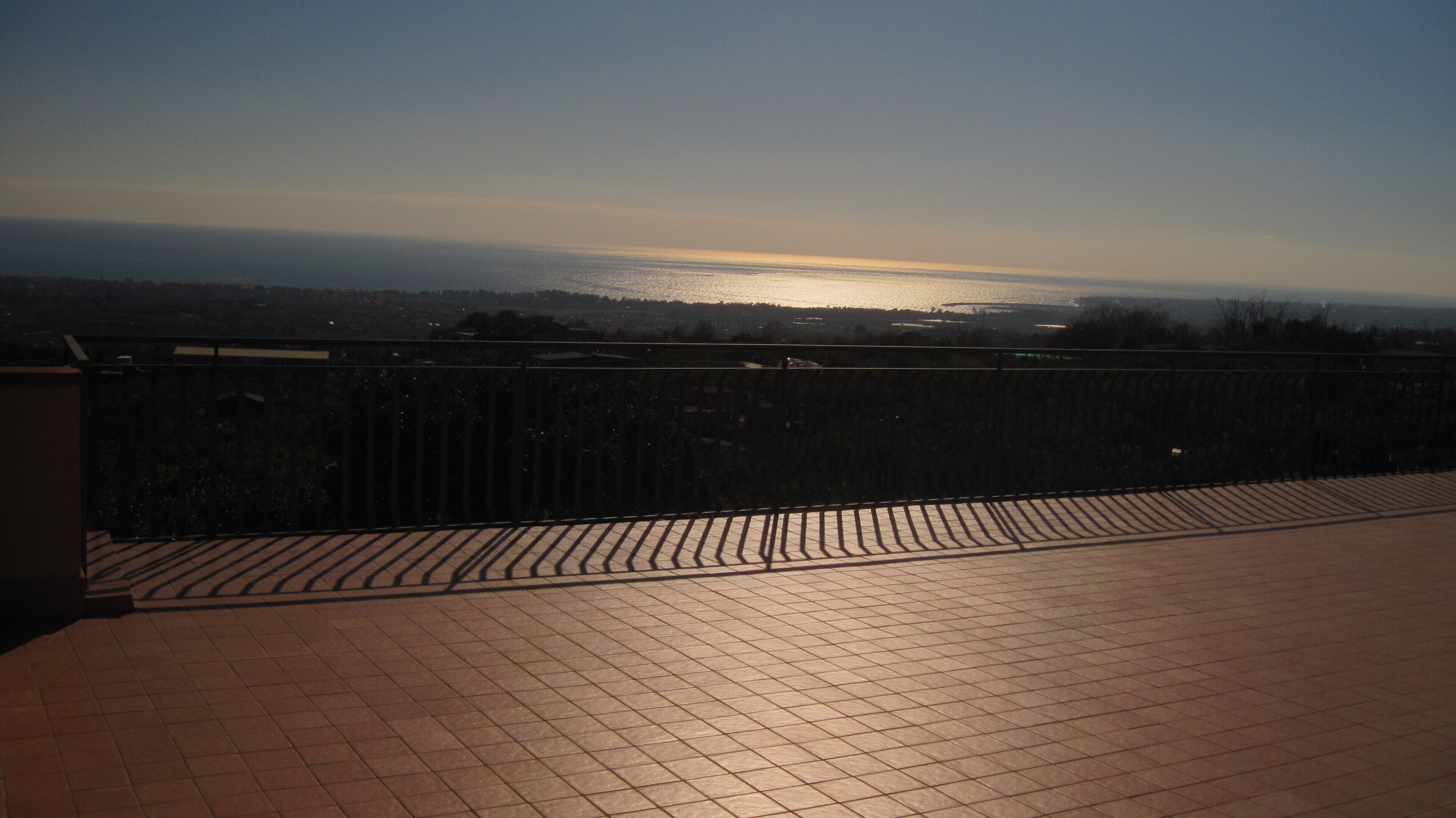 Un balcon carrelé offrant une vue sur une étendue d’eau et sur la terre ferme au loin.