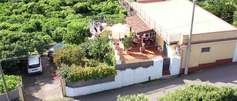 Un edificio con techo plano, balcón y zona pavimentada con plantas en macetas.