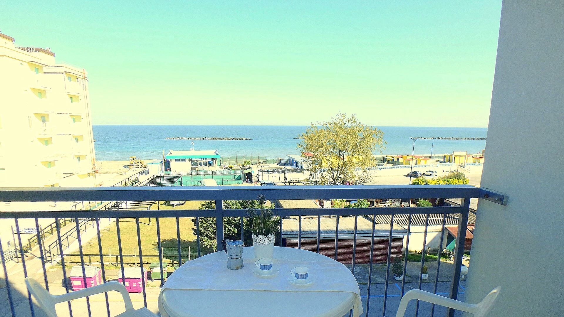 Un balcón con mesa y sillas, con vistas a una playa y edificios.