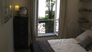 A bedroom with a bed, a dresser, a window with a view of greenery, and a lamp on the dresser. - Apartment/ flat - Paris (Paris)