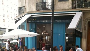 An outdoor café with patrons seated at tables under umbrellas, with a street and buildings in the background. - Apartment/ flat - Paris (Paris)