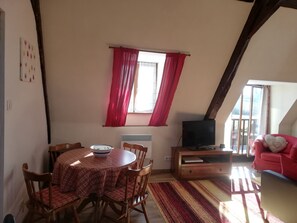 A cozy living room with a dining table, chairs, a television, and a red sofa.