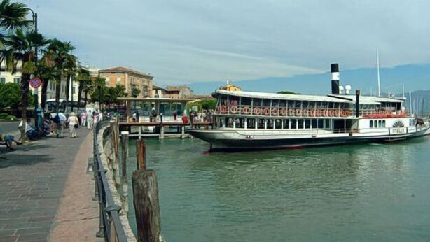A riverboat docked at a pier with a cityscape in the background.