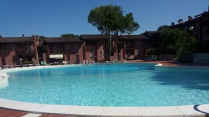 A swimming pool with a tiled deck, surrounded by buildings with balconies and a tree.