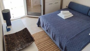 Een slaapkamer met een bed, een televisie op een dressoir, een raam en een deur die leidt naar een balkon.
