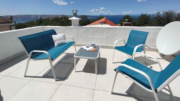Een terras met een bank, twee stoelen, een tafel en een schotelantenne.