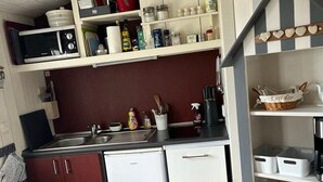 Una cocina compacta con armarios blancos, un microondas, un lavamanos y un refrigerador pequeño. Hay estantes sobre la encimera con distintos utensilios de cocina.