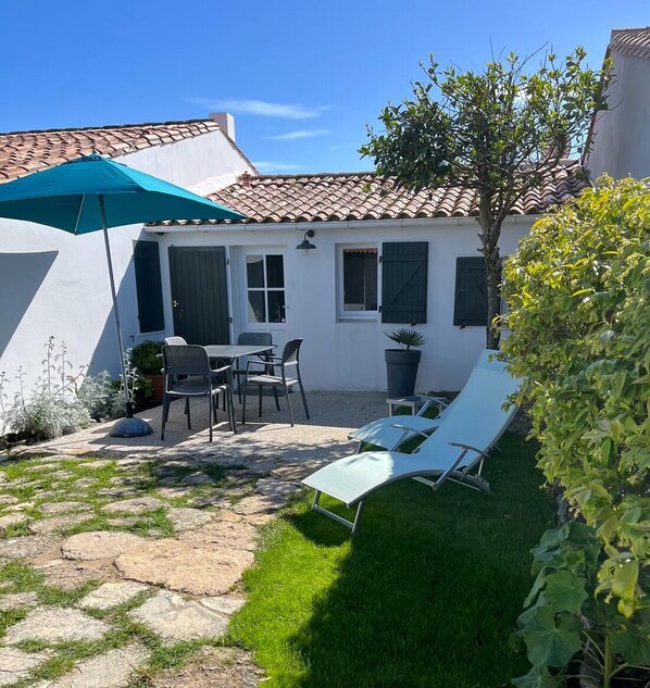 A patio with a table and chairs, a blue umbrella, and a small tree.