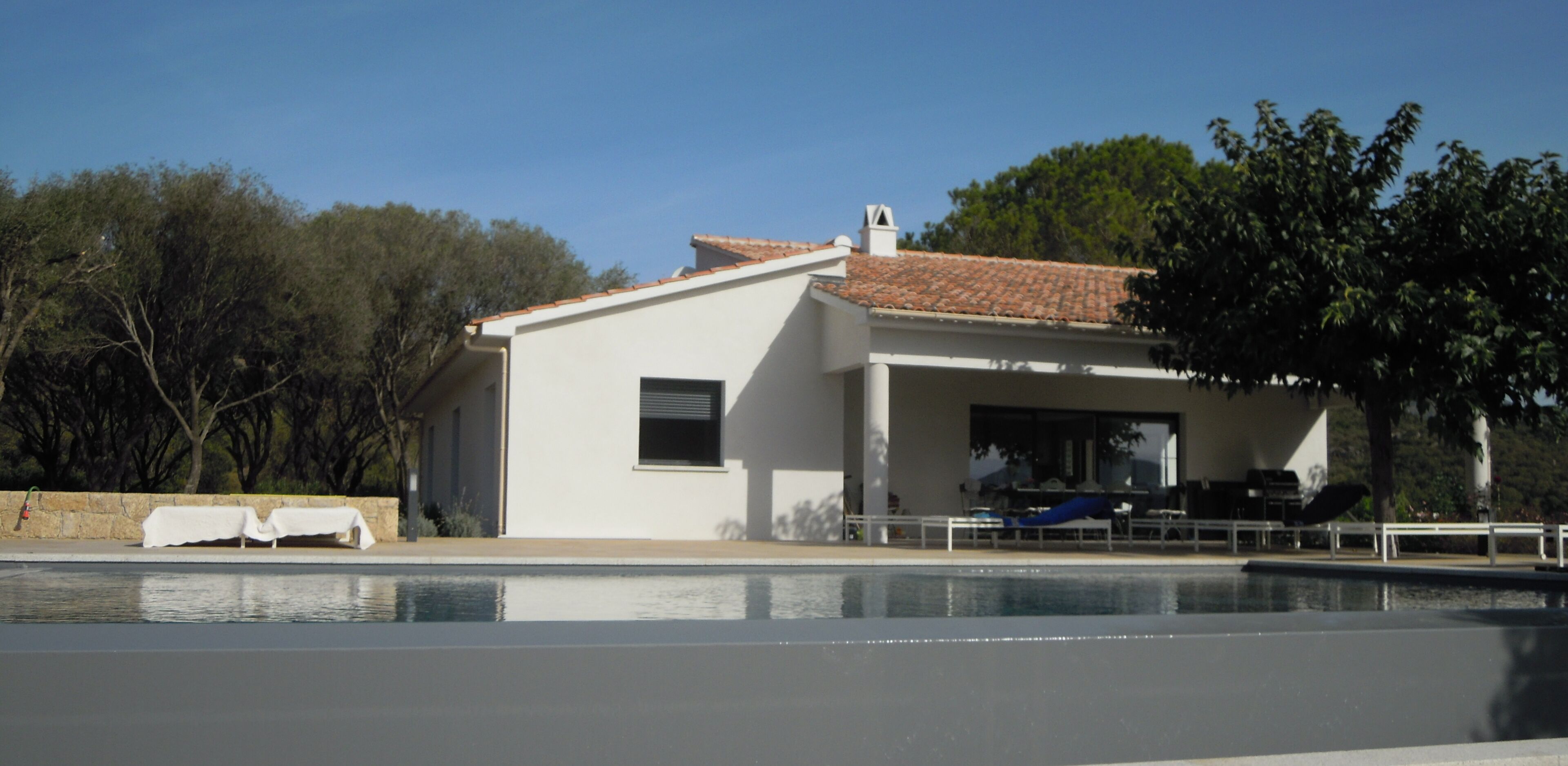 A modern house with a swimming pool, a covered patio, and a view of trees.