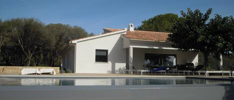 A modern house with a swimming pool, a covered patio, and a view of trees.