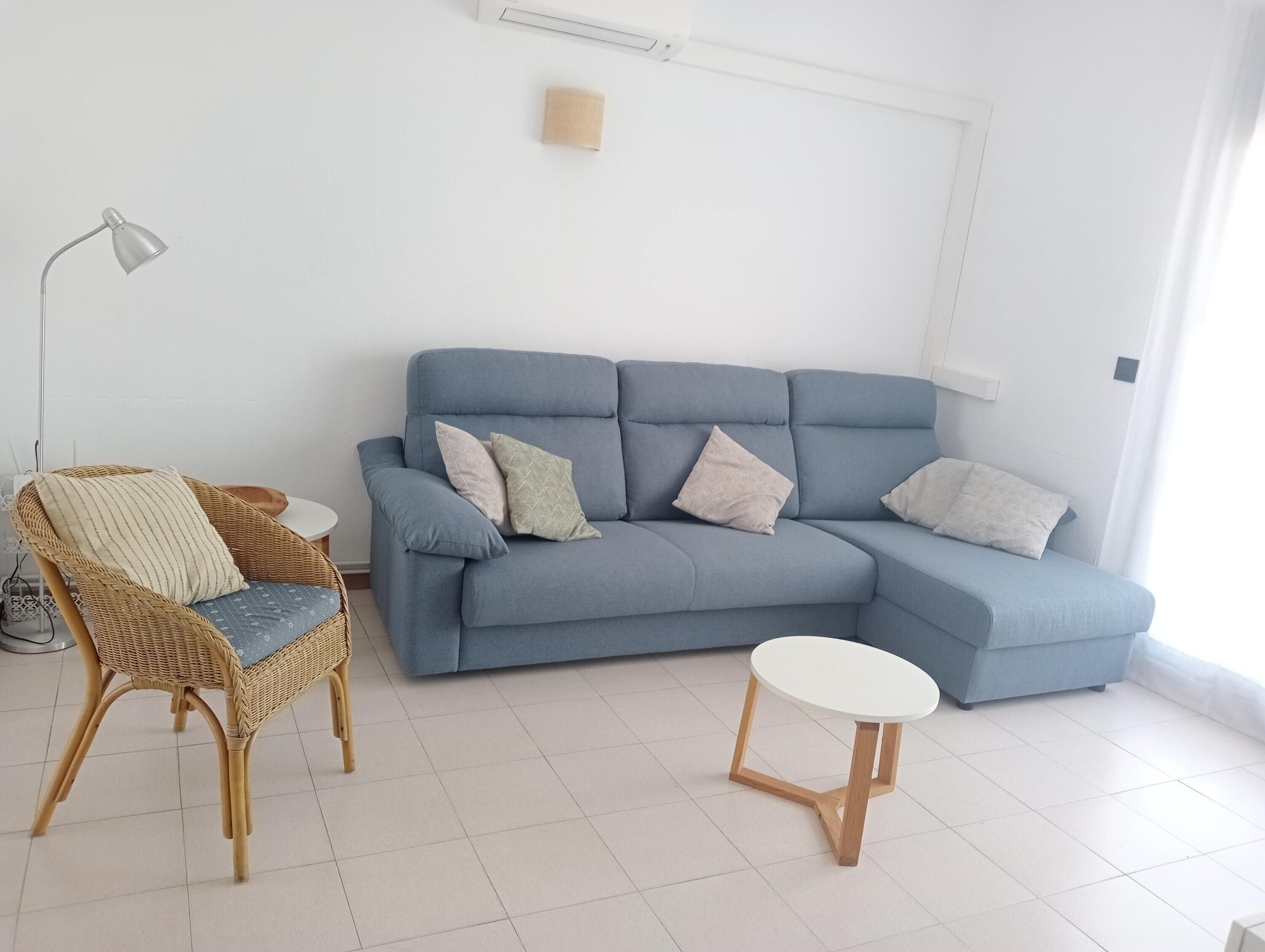 A living room with a blue sofa, a wicker chair, a small round table, and a floor lamp.