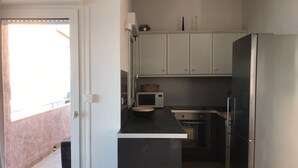 A compact kitchen with white cabinets, a black countertop, and a stainless steel refrigerator.