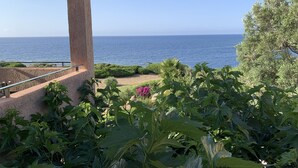 A terrace with a view of the sea, surrounded by greenery and a building structure.