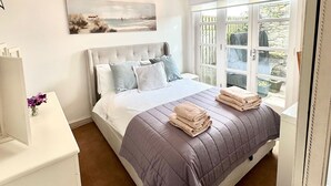 Un dormitorio con una cama grande, una araña, un cuadro y una ventana con vista a la vegetación.