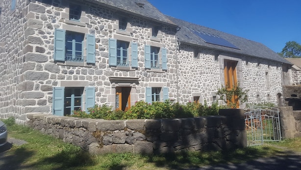 A stone building with multiple windows and shutters, a sloped roof, and a small garden area. - GRAND FERME AVEC PISCINE INTERIEURE ET SALLE DES JEUX (Virargues)