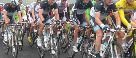 Un groupe de cyclistes en mouvement, portant différents maillots d’équipe et des casques, sur une route asphaltée.