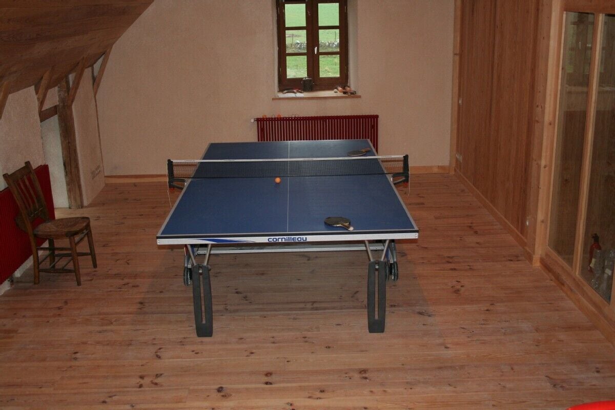 Une table de ping-pong dans une pièce dont le sol est en bois et qui possède une fenêtre.