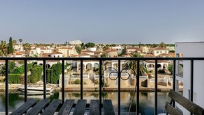 A balcony with a view of a town, including buildings, a body of water, and a palm tree. - Newly renovated apartment on the canals (Empuriabrava)