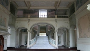 A grand staircase with ornate railings and a high ceiling with decorative moldings.