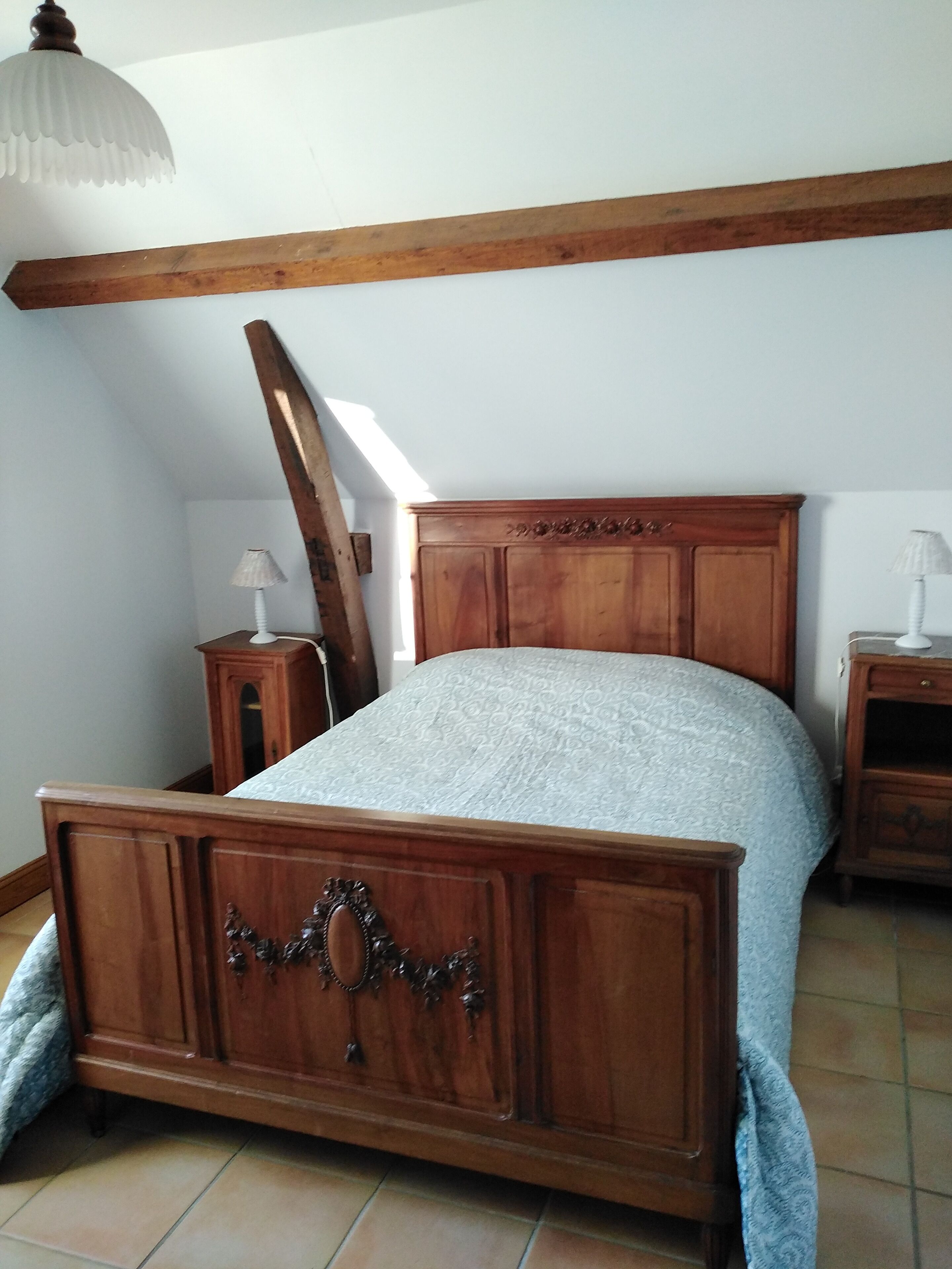 A bedroom with a wooden bed, a nightstand, a lamp, and a slanted ceiling.