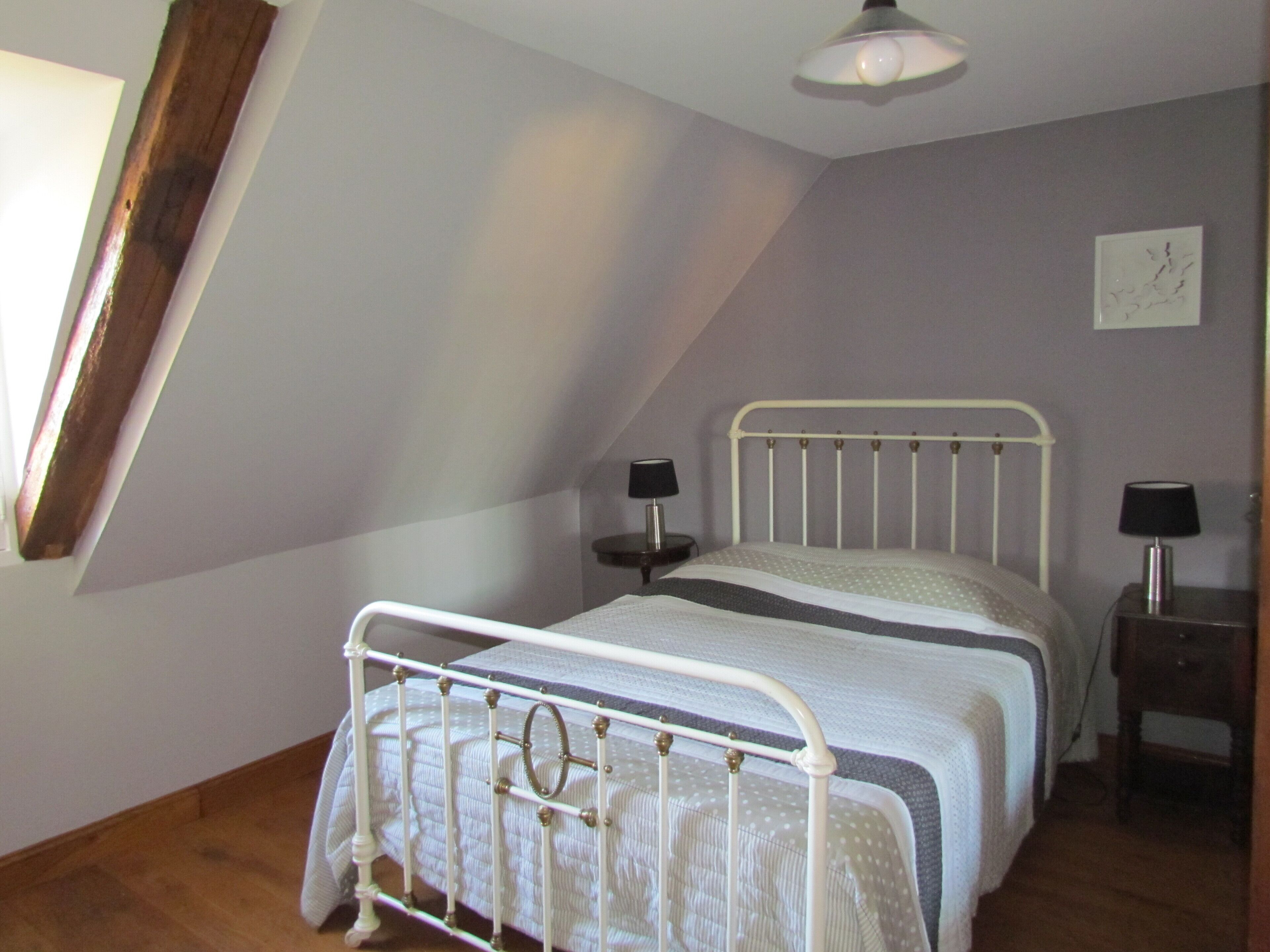 A bedroom with a sloped ceiling, a bed with a metal frame, two bedside tables with lamps, and a wall-mounted artwork.
