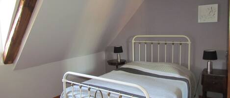A bedroom with a sloped ceiling, a bed with a metal frame, two bedside tables with lamps, and a wall-mounted artwork.