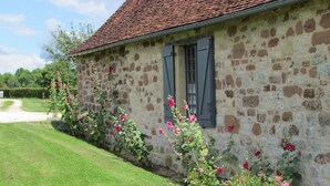 Een stenen gebouw met een rode dakbedekking, een raam met luiken en een tuin met roze bloemen.