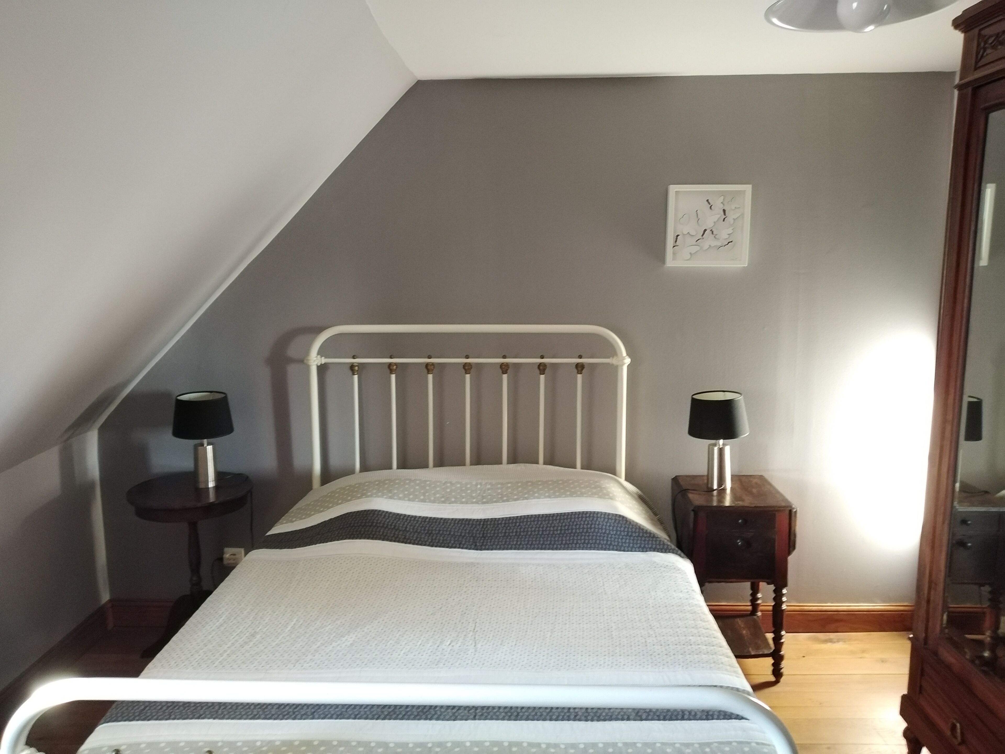 A bedroom with a white metal bed, two bedside tables with lamps, a wooden dresser, and a framed artwork on the wall.