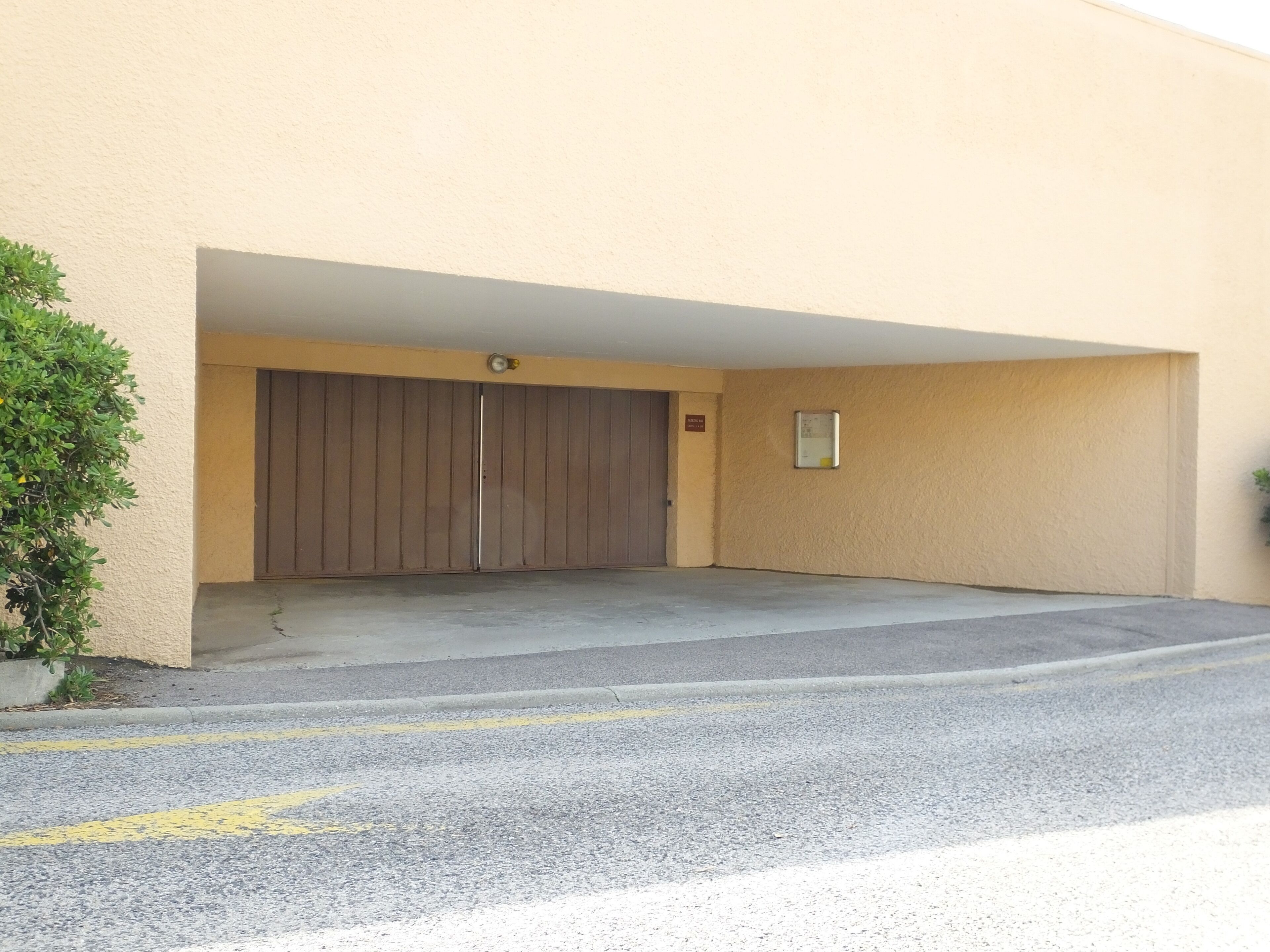 Entrada de un estacionamiento con puerta cerrada, un letrero pequeño y una cámara de seguridad.
