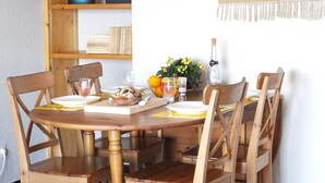 A wooden dining table with six chairs, a loaf of bread, a bottle of water, and a vase with flowers. - Collioure Seafront Apartment with Parking - Falco (Collioure)