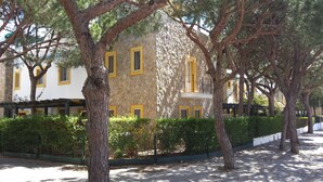 A building with stone walls and yellow window frames, surrounded by trees and a paved walkway. - Cozy Villa, Praia Verde, Algarve (Praia Verde)