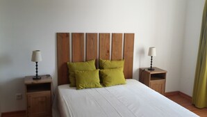 A neatly made bed with a wooden headboard, two bedside tables with lamps, and a green curtain. - Cozy Villa, Praia Verde, Algarve (Praia Verde)