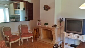A living room with a fireplace, a television, and two chairs. - Cozy Villa, Praia Verde, Algarve (Praia Verde)