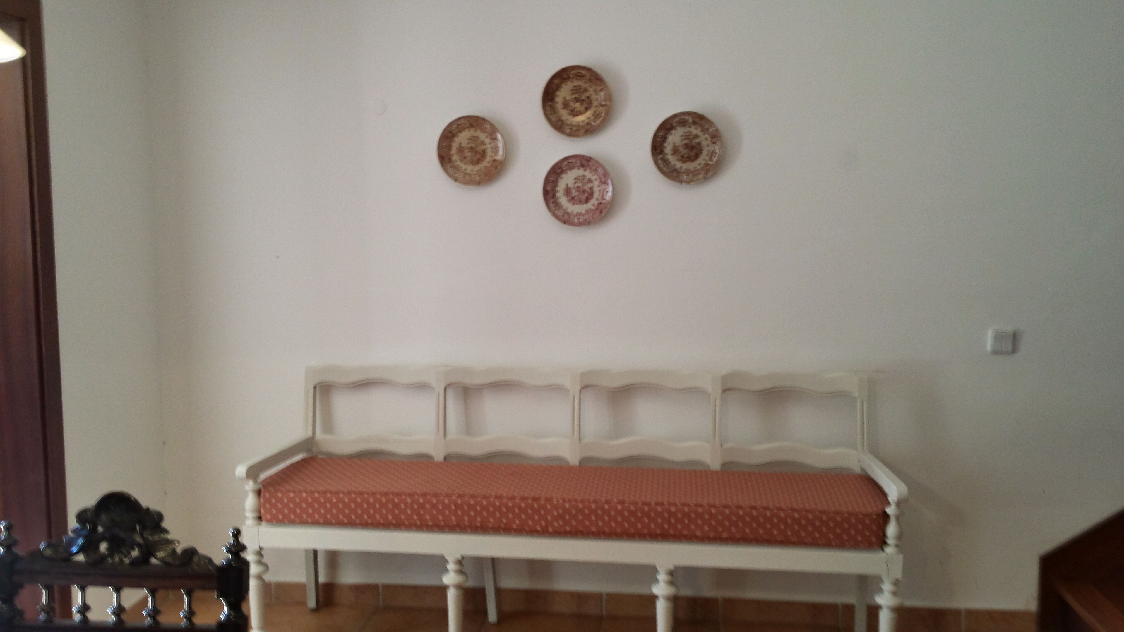 A white bench with a red cushion in a room with a white wall and four decorative plates above it.