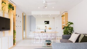 Uma sala de estar moderna com um sofá cinzento, uma mesa de centro de vidro e uma TV de tela plana fixada numa parede de madeira.